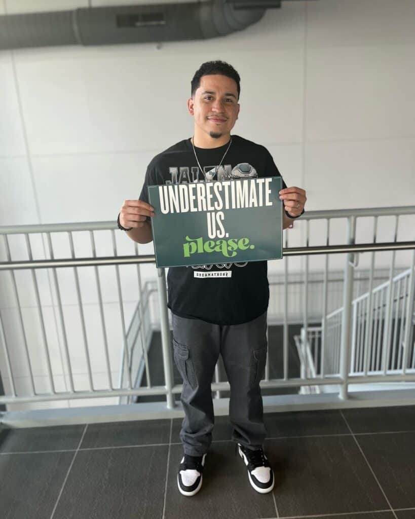 Anthony Ramos (underserved) holding underestimate us sign